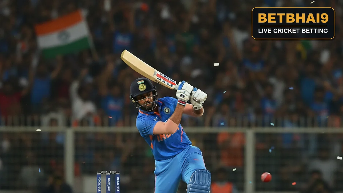 An Indian batsman in blue jersey playing a cover drive under floodlights in a packed cricket stadium